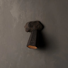 A dark textured stone sconce wall light with a geometric cone shade, mounted on a textured gray plaster wall.
