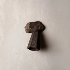 A rustic, dark brown metal and stone wall sconce shaped like a stylized head, mounted on a textured off-white plaster wall.