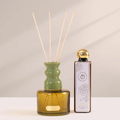 Natural reed diffuser set with a translucent amber glass refill bottle, a olive ceramic reed holder, and four natural reed sticks.