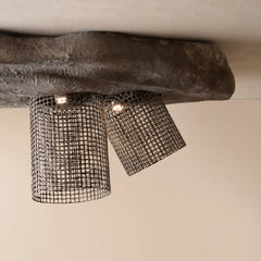 A rustic industrial-style ceiling light fixture with two cylindrical black wire mesh shades hanging below a thick, textured dark gray wooden beam.