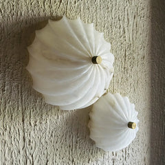 Unique decorative two white wall sconces with gold centers on a textured beige wall.
