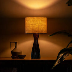 Garnet Table Lamp with a textured shade on a dark surface, casting a warm glow.