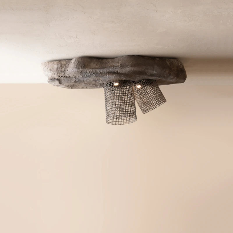 A rustic industrial ceiling light fixture with a rough, organic-shaped dark gray stone base and two cylindrical metal mesh shades