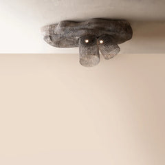 A rustic ceiling light fixture with a rough, organic-shaped dark gray stone or concrete base and two hanging cylindrical mesh shades