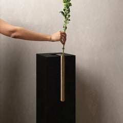 Decorative Bookcase Vase with a vertical brushed brass cylinder insert, shown with a person's arm placing a green flower stem into it.