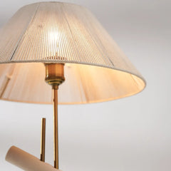 Close-up of a lamp with a beige shade and brass base on a light gray background