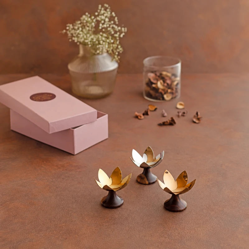 Lotus Blossoms _ Gift Box, three brass lotus tealight holders on dark wood bases beside open pink gift box