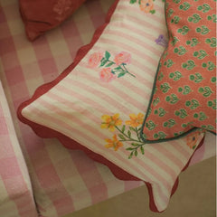 Rosalia Dusty Rose Linen Oblong Cushion Cover beside red buti print cushion on gingham armchair