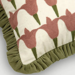 Close-up of a decorative throw pillow featuring a textured pink tulip pattern on an off-white background, finished with an olive green ruffled border.