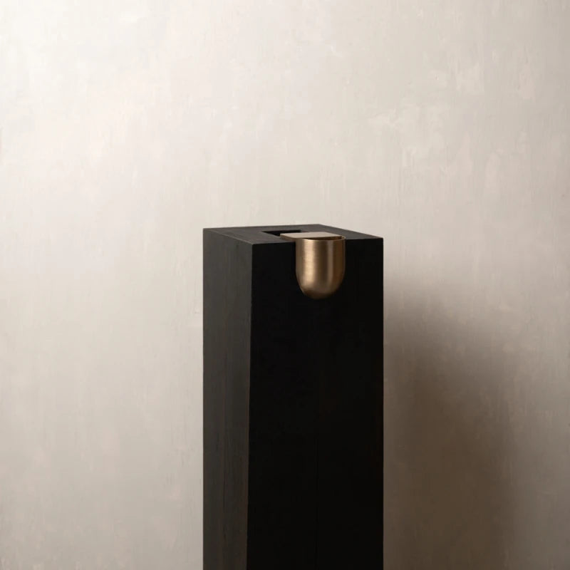 A modern black Bookcase Vase with a brushed brass dome accent on the front, set against a textured light gray wall.