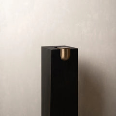 A modern black Bookcase Vase with a brushed brass dome accent on the front, set against a textured light gray wall.