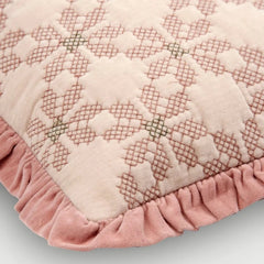 A close-up of a quilted throw pillow featuring a dusty pink and cream floral pattern with a ruffled pink velvet border.
