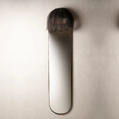 A long wall mirror with a long, narrow oval shape and a dark, textured, shaggy top section.