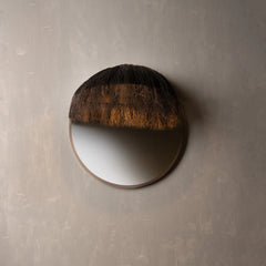 A round wall mirror with a dark brown textured fur or straw-like top.