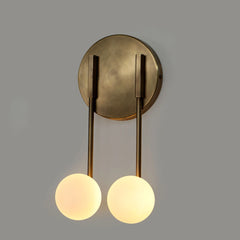 Brass loop wall sconce with two arms and illuminated glass globes on a gray background