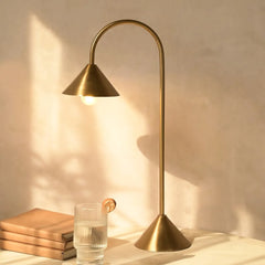 Gold table lamp on a surface with a glass of water and books in soft lighting.