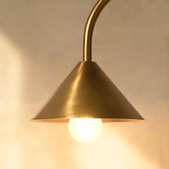 Hush Table Lamp with gold cone shade, casting a warm glow on a beige background