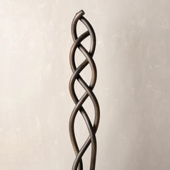 A dark bronze twisted metal decorative sculpture or architectural accent, shown vertically against a textured light beige background.