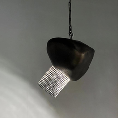 A modern pendant light with a dark, organic-shaped shade and a cylindrical mesh shade covered in small clear rhinestones, hanging from a black chain against a neutral gray background.