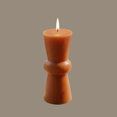 A single lit taper candle (Non Scented) in a warm terracotta or burnt orange color, standing upright against a solid taupe-gray background. 