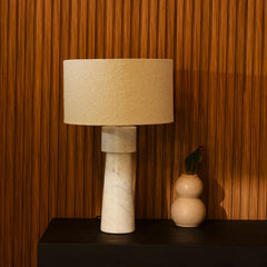 Loam Table Lamp with beige shade and marble base on a dark surface against a wooden wall.