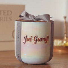 A personalized U-Glass candle in a white ceramic jar with an iridescent finish, featuring the name 'Jai Guruji' in rose gold lettering and wrapped in a gray ribbon with a bow.
