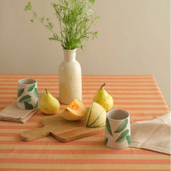 Linea Ruffle Amber Cotton Table Cover styled with pears, melon, leaf-print cups and vase, front view
