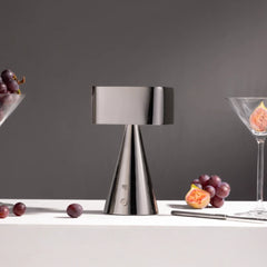 Silver table lamp made of metal on a white surface with grapes and a glass in the background