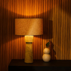 Decorative Loam Table Lamp with a textured fabric shade on a marble base next to a small plant against a wooden paneled wall.