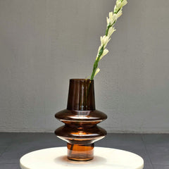 Brown Ripple Glass Vase with a single white flower on a gray surface and background