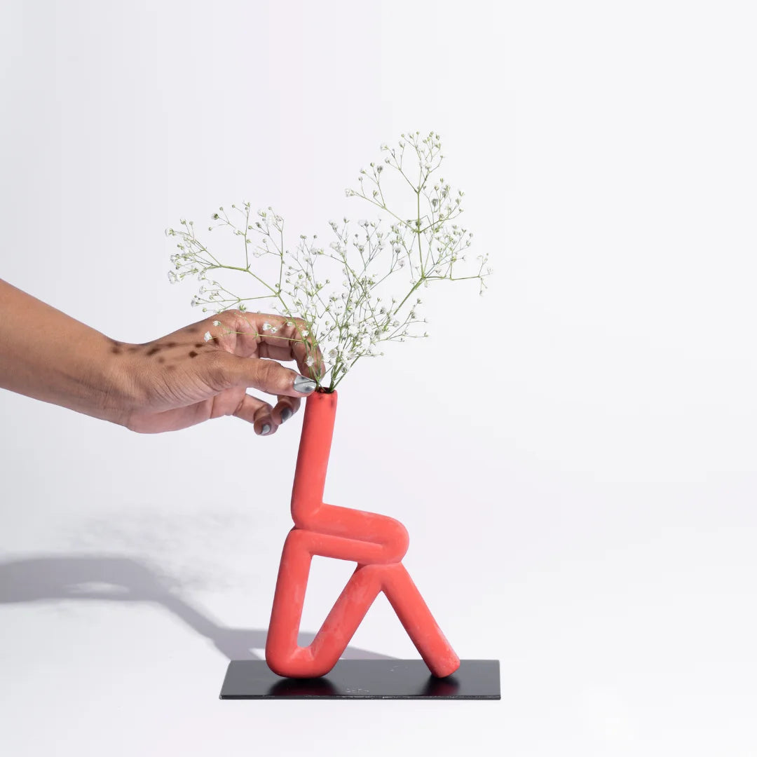 Person placing flowers into a unique red vase shaped like a person on a white background