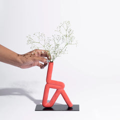Person placing flowers into a unique red vase shaped like a person on a white background