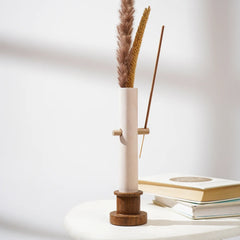 Decorative vase with wooden base and dried plants on a white surface