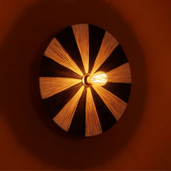 Unique Fiore wall lamp with black and natural color circular design in raffia, casting warm glow.