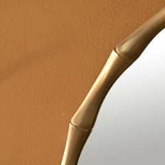 Close-up of a lune mirror in gold bamboo-inspired handle on a textured surface