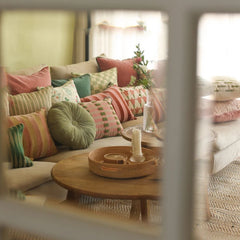 A cozy living room scene with a light beige sofa styled with multiple colorful throw pillows in pink, green, beige, Cuddle Fern Velvet Round Cushion, and striped patterns.