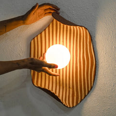 Hand holding a glowing light bulb inside a hexagonal wooden lamp with stripes