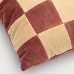 A close-up of a square throw pillow featuring a checkered pattern in dusty rose and beige velvet fabric, shown on a light gray background.