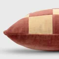 A close-up of a square throw pillow with a checkered patchwork design in dusty rose velvet and beige linen fabric, shown against a light gray background.