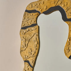 Close view of wall mirror with textured gold frame on a beige wall