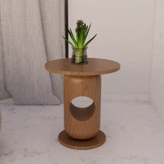 A round wooden side table with a cylindrical base, featuring a circular cutout in the middle and a matching round base. A small green potted plant sits on top.