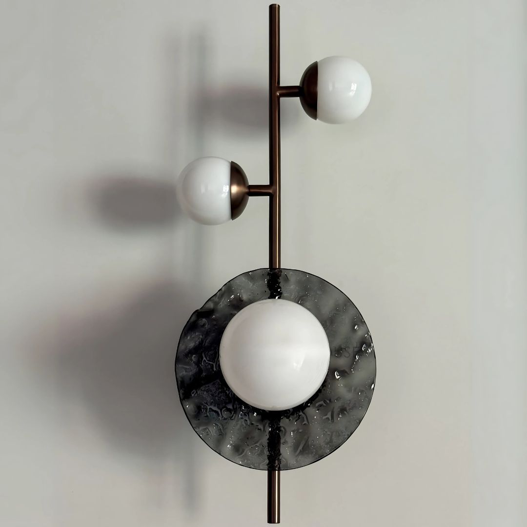 A wall sconce featuring a vertical metal rod with two white opaline glass globes on either side, and a larger slumped glass circle in the center.