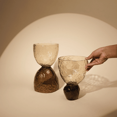 Two textured glass decorative objects of different sizes, with a hand lifting one of the objects.