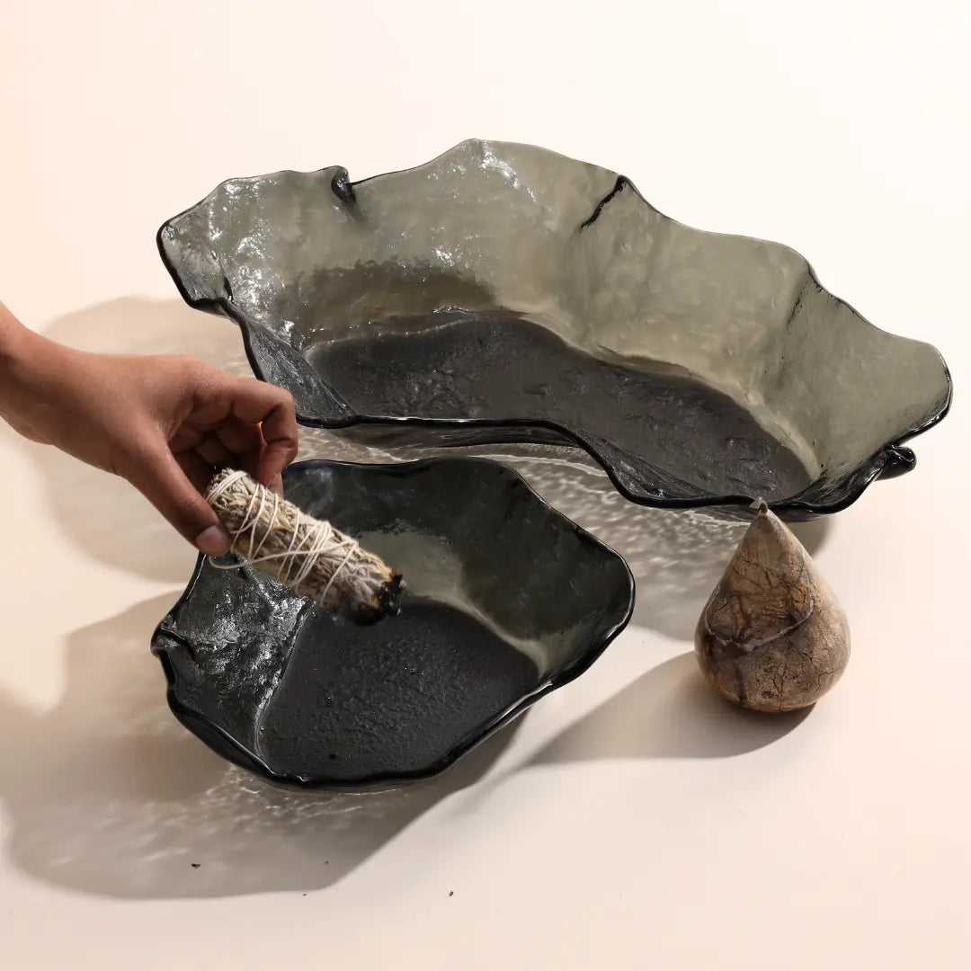 Lava glass bowls on a light background with a hand holding a bundle of sage.