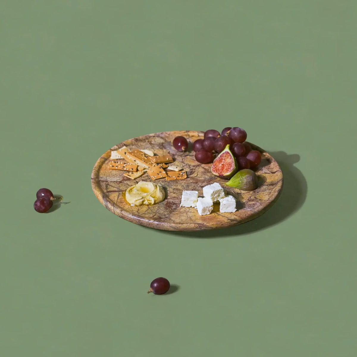 Wooden plate with cheese, crackers, and fruits on a green background