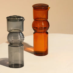 Two Coil Glass Carafe, one gray and one amber, on a beige background