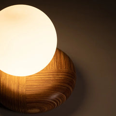 Close view of wooden wall light fixture with a glowing glass white bulb on a dark background