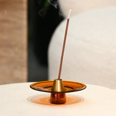 Incense stick burning in an amber-colored holder on a white surface with a blurred background