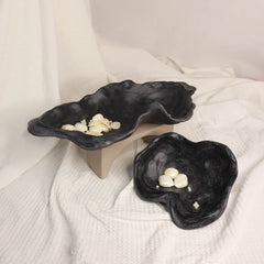 Two black ceramic organic bowls with a swirled edge design, displayed on a white textured surface.