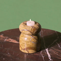 Decorative stone candle holder with a lit candle on a marble surface against a green background